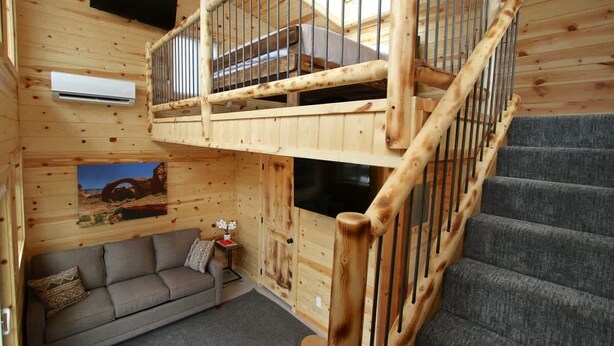 A cabin interior with a wooden staircase, a sofa, and a mounted television.