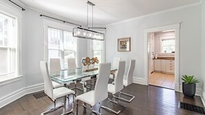A modern dining area with a glass table, white chairs, and a pendant light. -  A luxury and modern estate. Free airport transfer with Tesla Model X! (Peoria)