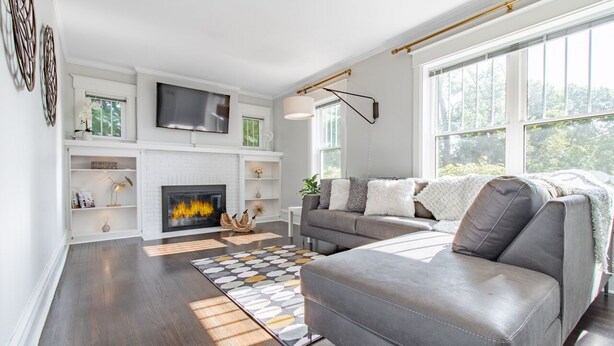 A modern living room with a fireplace, a grey sofa, and a large window providing a view of the outdoors. -  A luxury and modern estate. Free airport transfer with Tesla Model X! (Peoria)