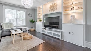 A modern living room with a large flat-screen TV, white cabinetry, and a chandelier. -  A luxury and modern estate. Free airport transfer with Tesla Model X! (Peoria)
