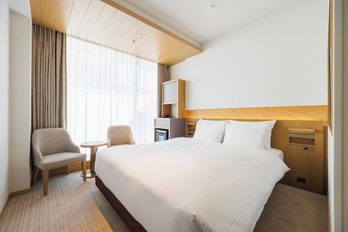 Quarto de hotel com uma cama grande, uma escrivaninha, uma cadeira e uma mesinha.