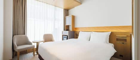 A hotel room with a large bed, a desk, a chair, and a small table.