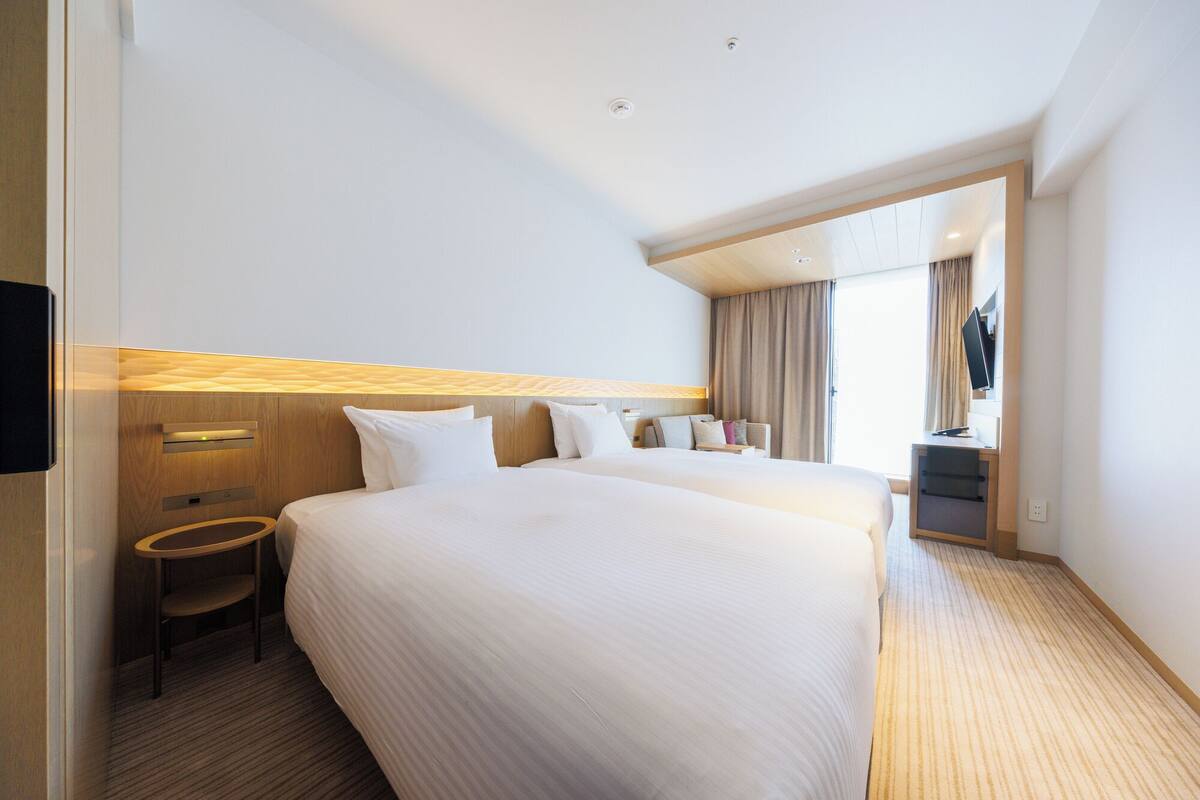 Quarto de hotel com duas camas, uma escrivaninha, uma cadeira e uma televisão.