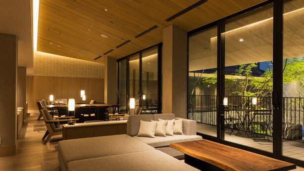 A modern living room with a sofa, a wooden coffee table, and a dining area with chairs and a table. - Hotel Metropolitan Kamakura (Kamakura)