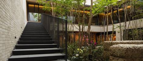 Un bâtiment moderne doté d’un escalier menant à un niveau supérieur, entouré de verdure et agrémenté d’éléments en pierre.