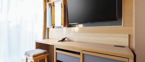 A modern hotel room with a wooden desk, a flat-screen TV, a chair, and a window with sheer curtains.