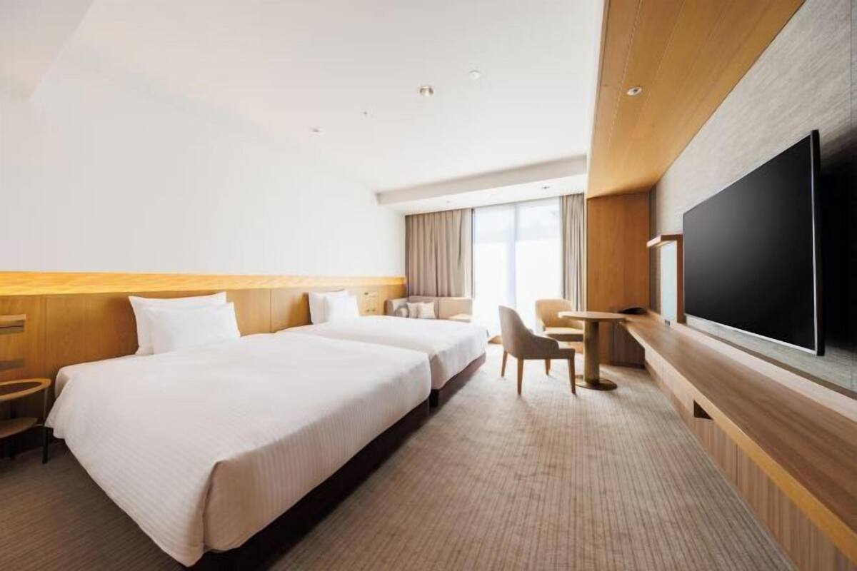 Quarto de hotel com duas camas, televisão, secretária e janela.