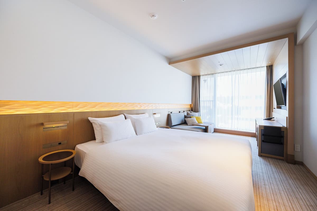 Quarto de hotel com uma cama grande, uma escrivaninha, uma cadeira e uma televisão.