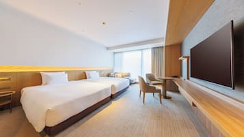 A hotel room with a large bed, a desk, a chair, a TV, and a window with curtains.