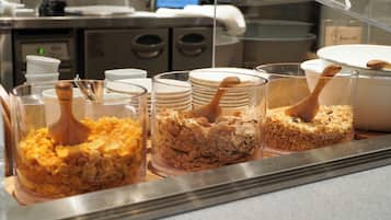 Un bufé con diversos alimentos en recipientes transparentes, incluyendo cereales y granola.