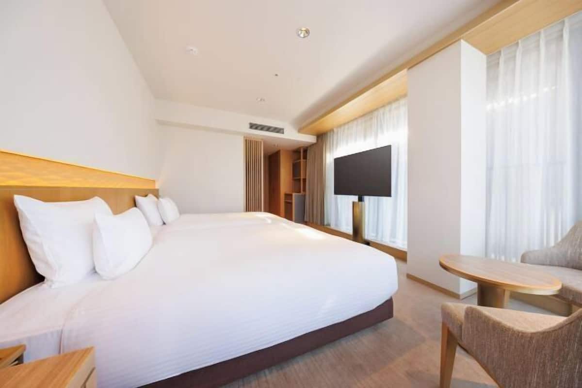 Quarto de hotel com uma cama grande, uma televisão, uma mesinha e uma cadeira.