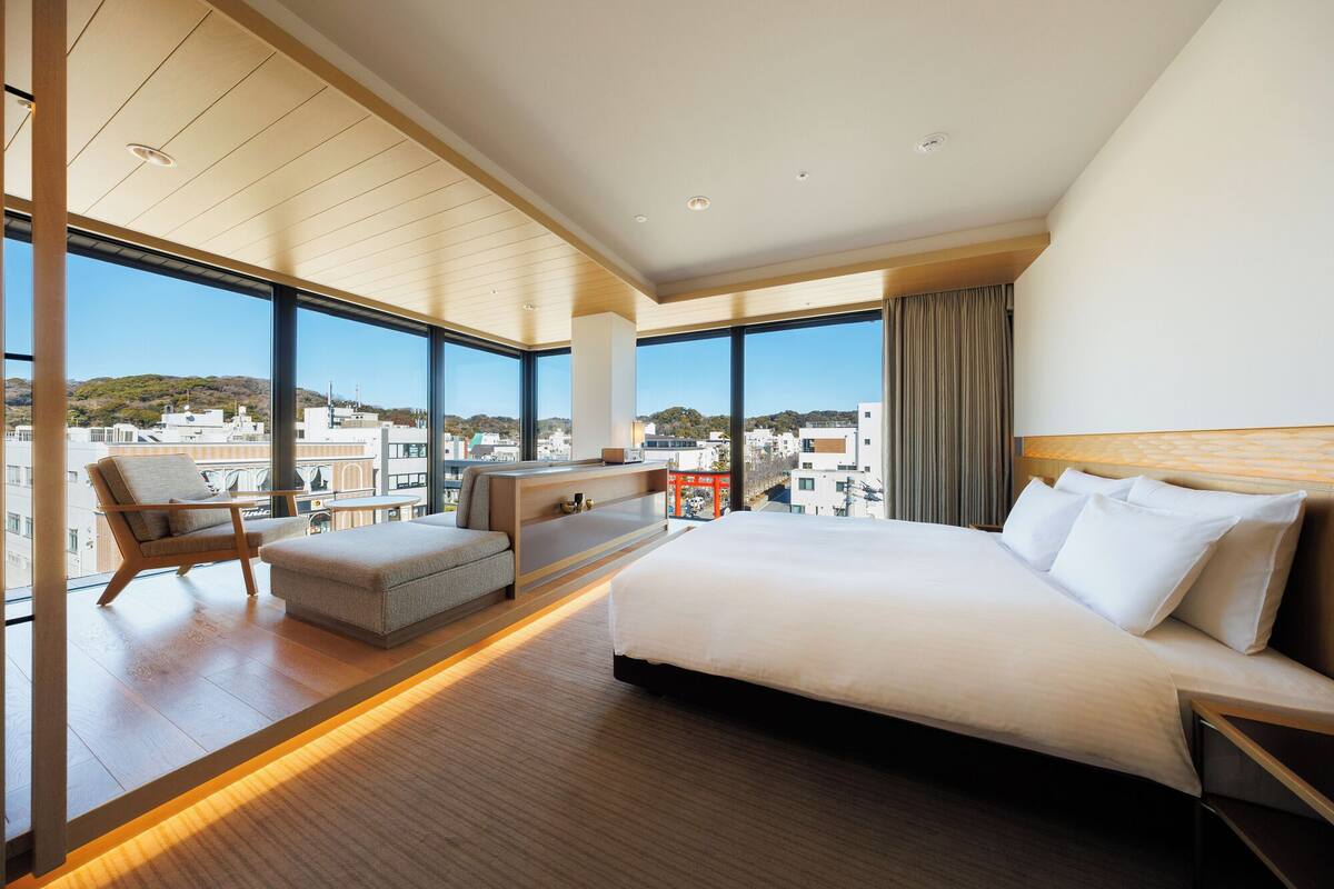 Quarto de hotel moderno com uma cama grande, área de estar e vista para a cidade.