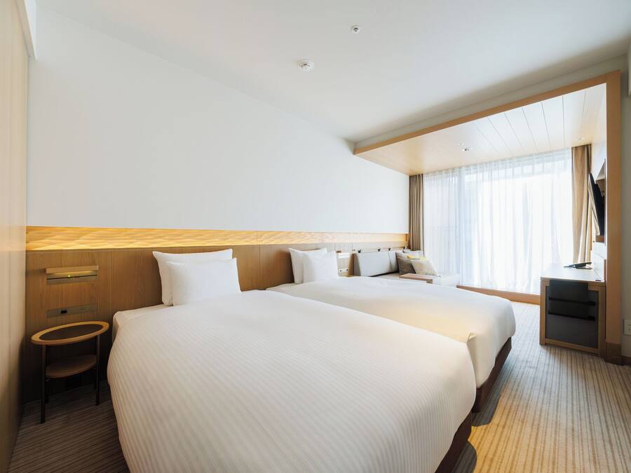 A hotel room with two beds, a desk, a chair, and a large window.