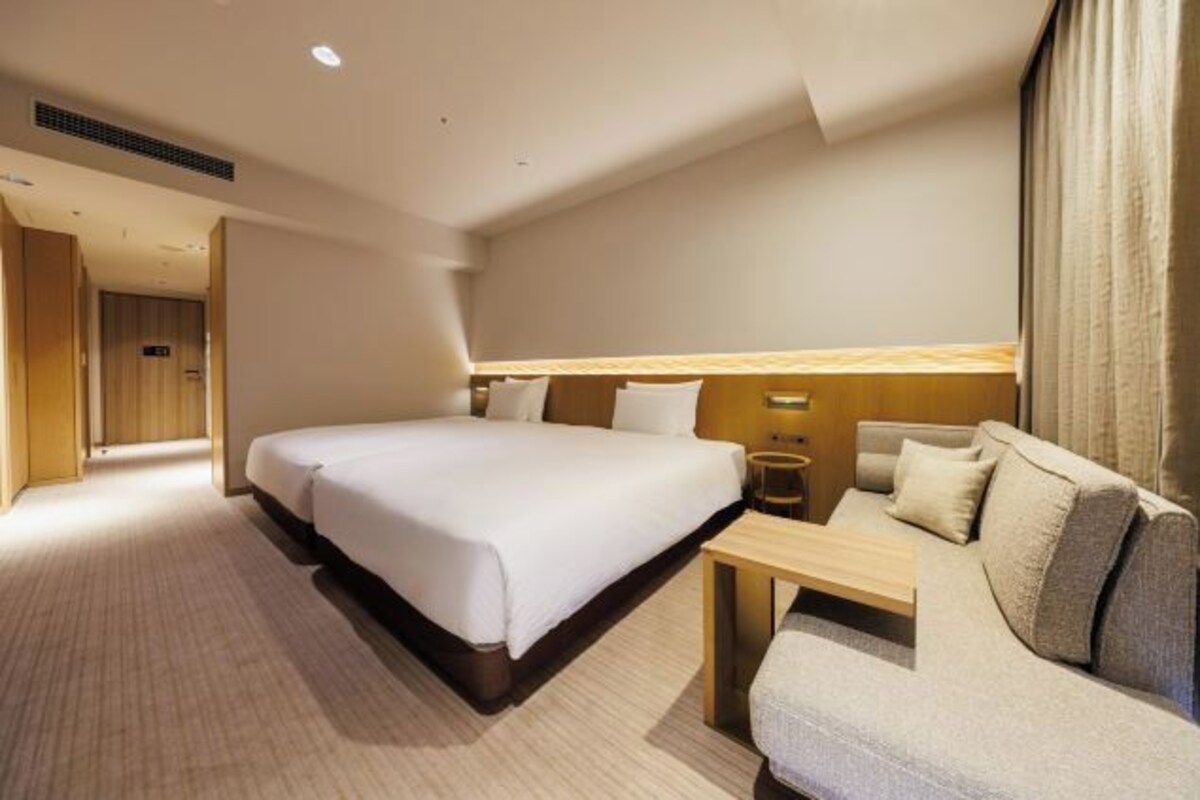 Una habitación de hotel con una cama grande, un sofá, una mesita y un cabecero de madera.