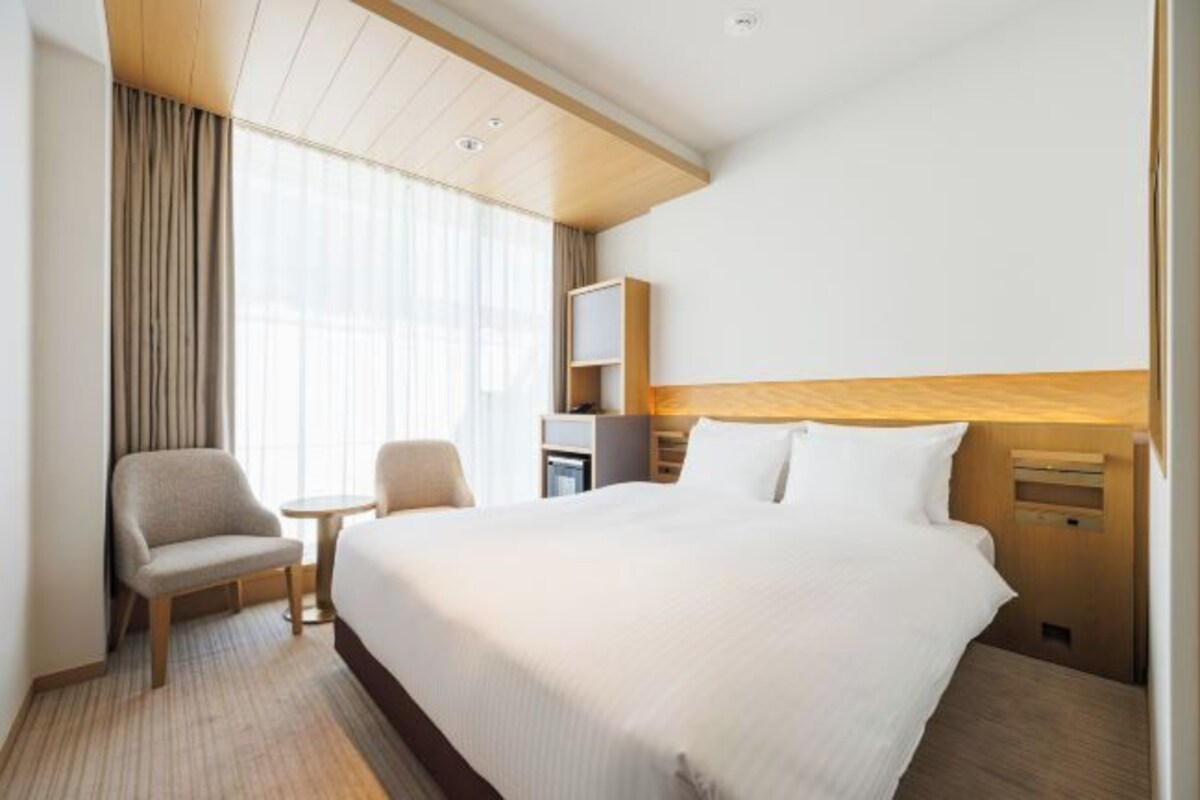 Habitación de hotel con una cama grande, una silla, una mesita, un televisor y un escritorio con lámpara.