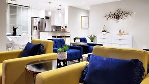 Een moderne woonkamer met gele en blauwe banken, een eethoek en een keuken.