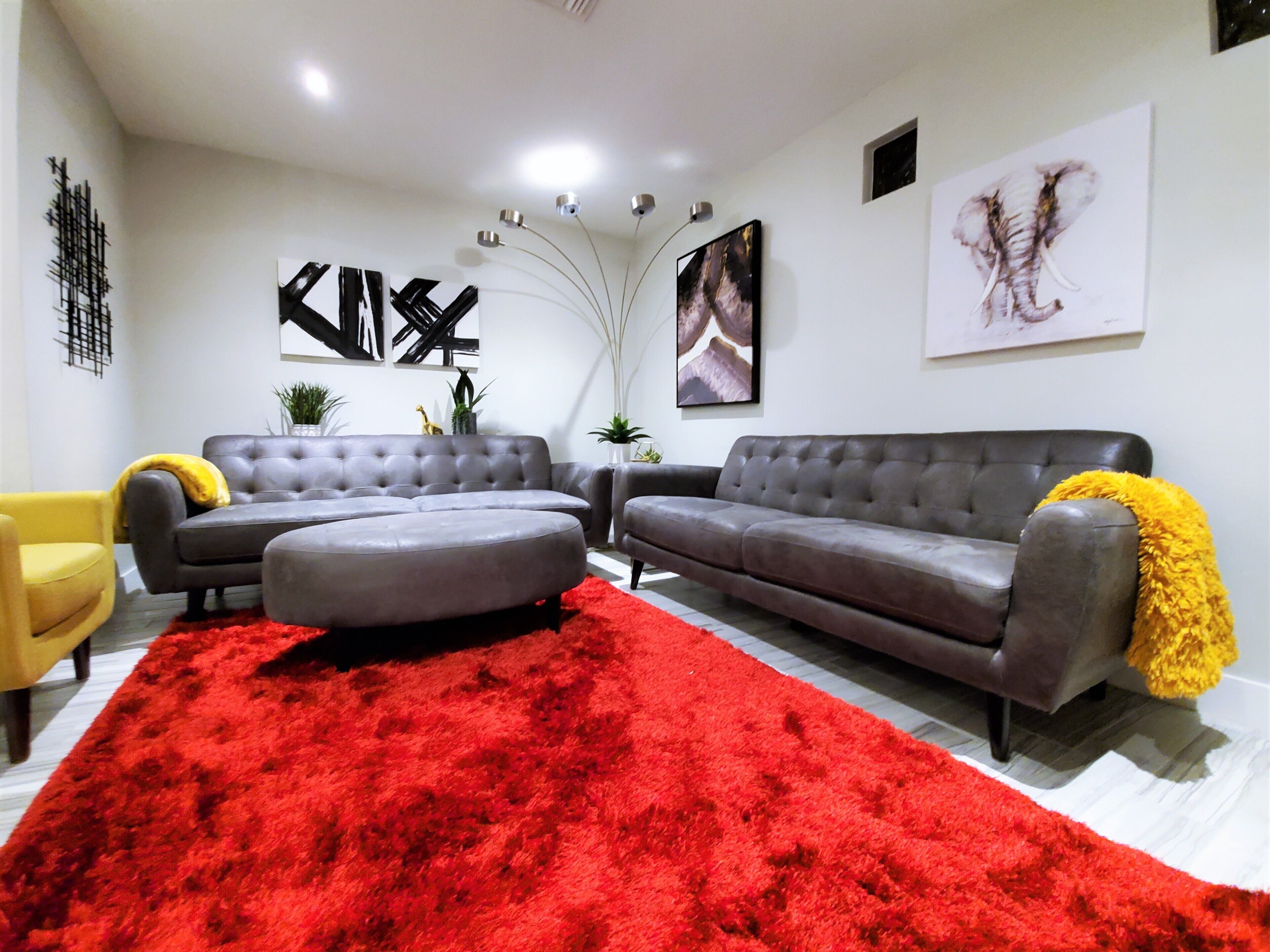 A modern living room with two grey sofas, a red shag rug, and a yellow armchair.