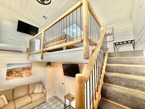 Une pièce de style loft avec un escalier en bois, un canapé, un téléviseur à écran plat et un tableau encadré au mur.