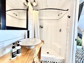A bathroom with a wooden vanity, a white sink, and a shower stall.