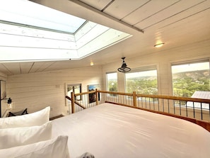 A bedroom with a skylight, a bed, a view of the landscape, and a balcony railing.