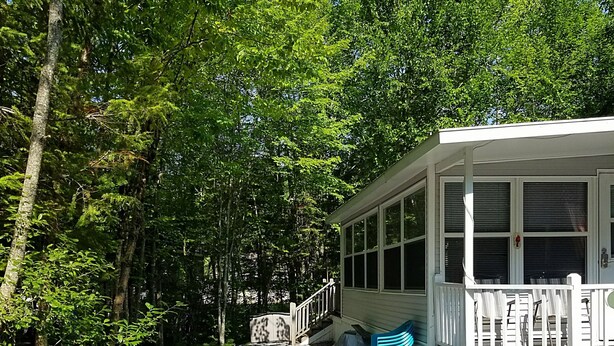 Un espace extérieur abrité avec un foyer, une véranda dotée d’une balustrade et un chemin de gravier traversant une zone boisée.