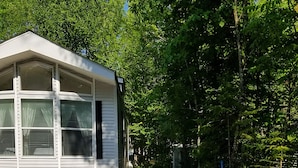 Une petite cabane à un seul étage, dotée d’un toit en pente, entourée de gravier et d’une forêt dense.