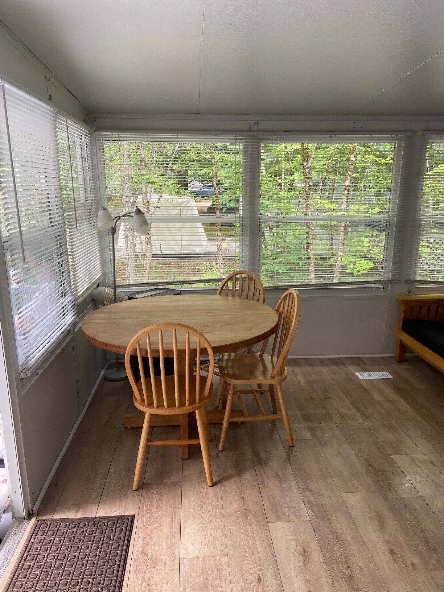 Une véranda avec une table et des chaises en bois, de grandes fenêtres et une vue sur la verdure environnante.