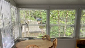Une véranda avec une table et des chaises en bois, de grandes fenêtres et une vue sur la verdure environnante.