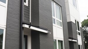 A modern two-story building with a grey and white exterior, large windows, and a small front porch area.