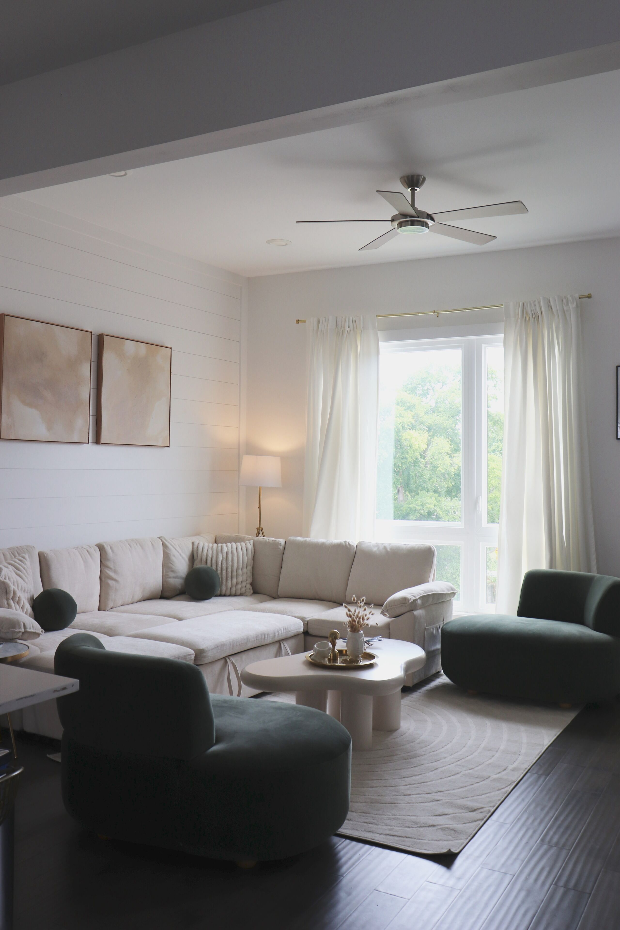 Un salon moderne avec un canapé d’angle, une table basse ronde et un ventilateur de plafond.
