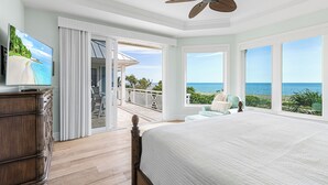 Ein Schlafzimmer mit einem großen Bett, einem Deckenventilator, einem Fernseher und einem Balkon mit Meerblick.