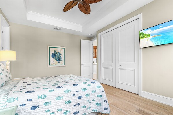 Un dormitorio con una cama, ventilador de techo, televisor y una puerta.