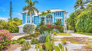 Ein zweistöckiges Haus mit blauer Fassade, umgeben von tropischer Vegetation und einem gepflegten Garten.
