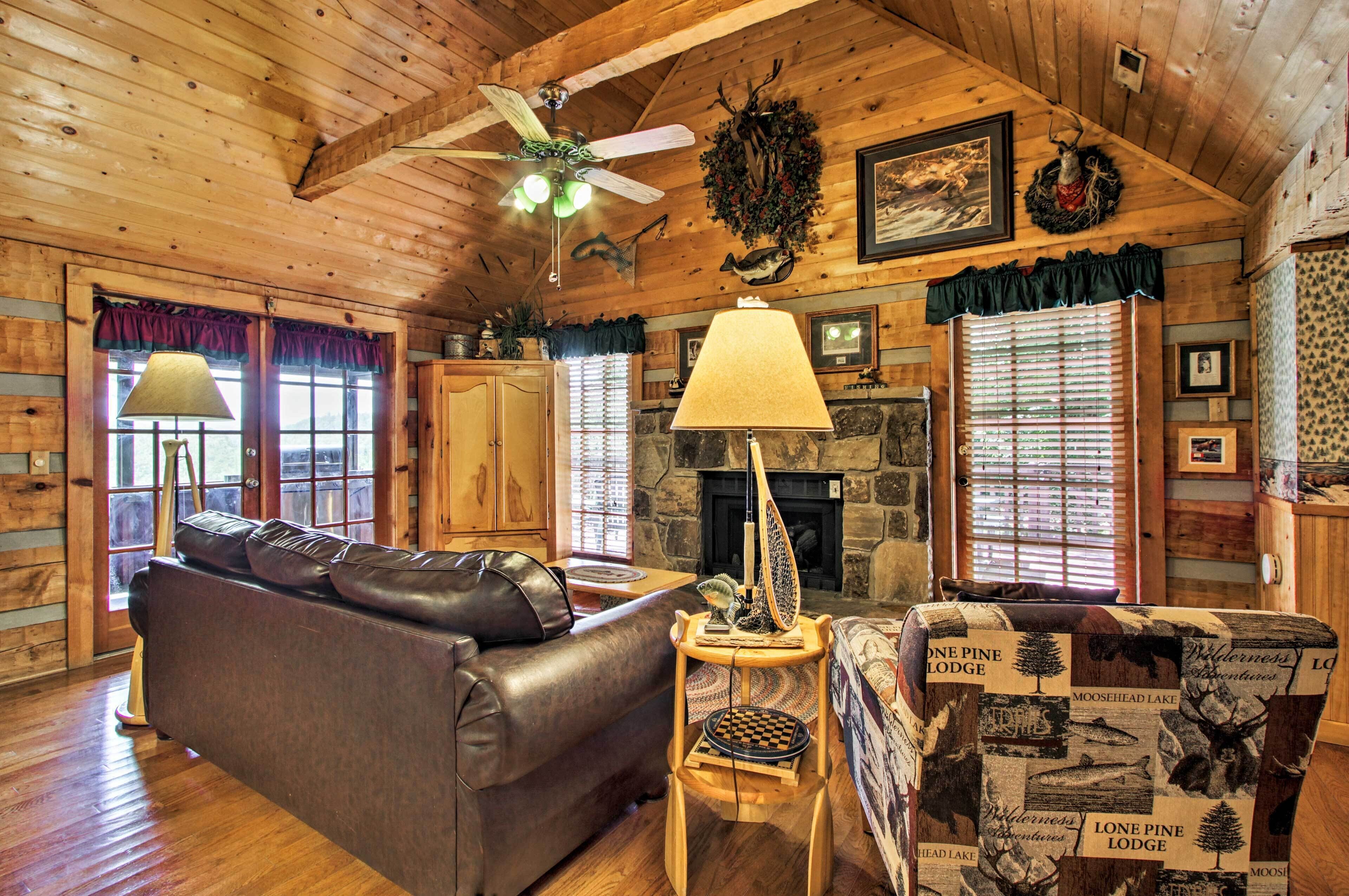 A cozy cabin interior with a leather sofa, a table with a lamp, a fireplace, and wooden walls.