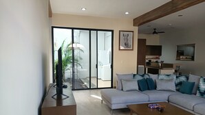 Uma sala de estar moderna com um sofá cinza, uma mesa de centro de madeira e uma televisão sobre um suporte.