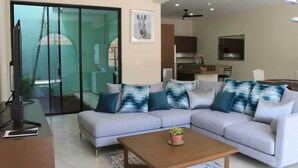 Uma sala de estar moderna com um sofá modular cinza, uma mesa de centro de madeira e uma porta de vidro que dá para uma varanda.