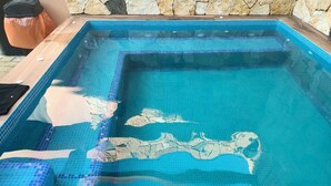 Uma piscina retangular com azulejos de mosaico azul e borda de deck de madeira.