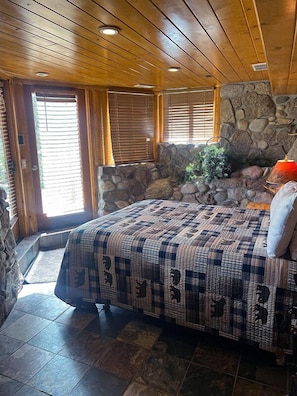 Un dormitorio acogedor con una cama grande, pared de piedra, techo de madera y una chimenea de piedra.