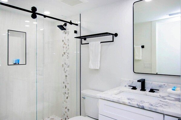 A modern bathroom with a glass shower enclosure, a marble sink, and a large mirror.