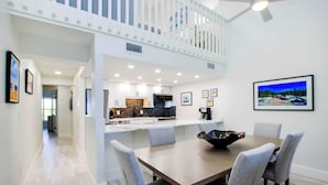 A modern kitchen with white cabinets, a black backsplash, and a dining area with a wooden table and grey upholstered chairs.