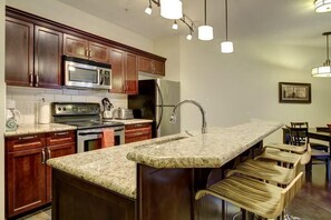 Una cocina con armarios de madera oscura, electrodomésticos de acero inoxidable, encimera de granito y una zona de bar con taburetes.