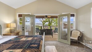 Un dormitorio con una cama grande, una mesita de noche, una lámpara y vistas a una terraza exterior con sillas y una mesa.