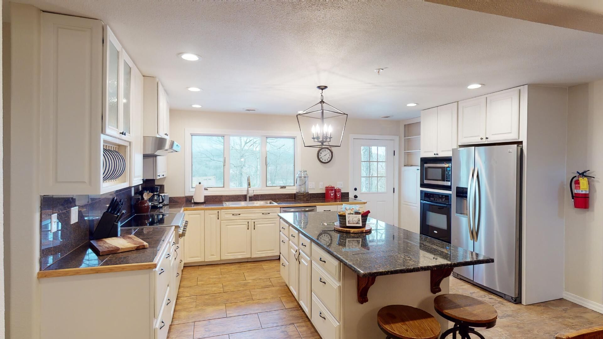 A modern kitchen with white cabinetry, a central island, stainless steel appliances, and a chandelier.