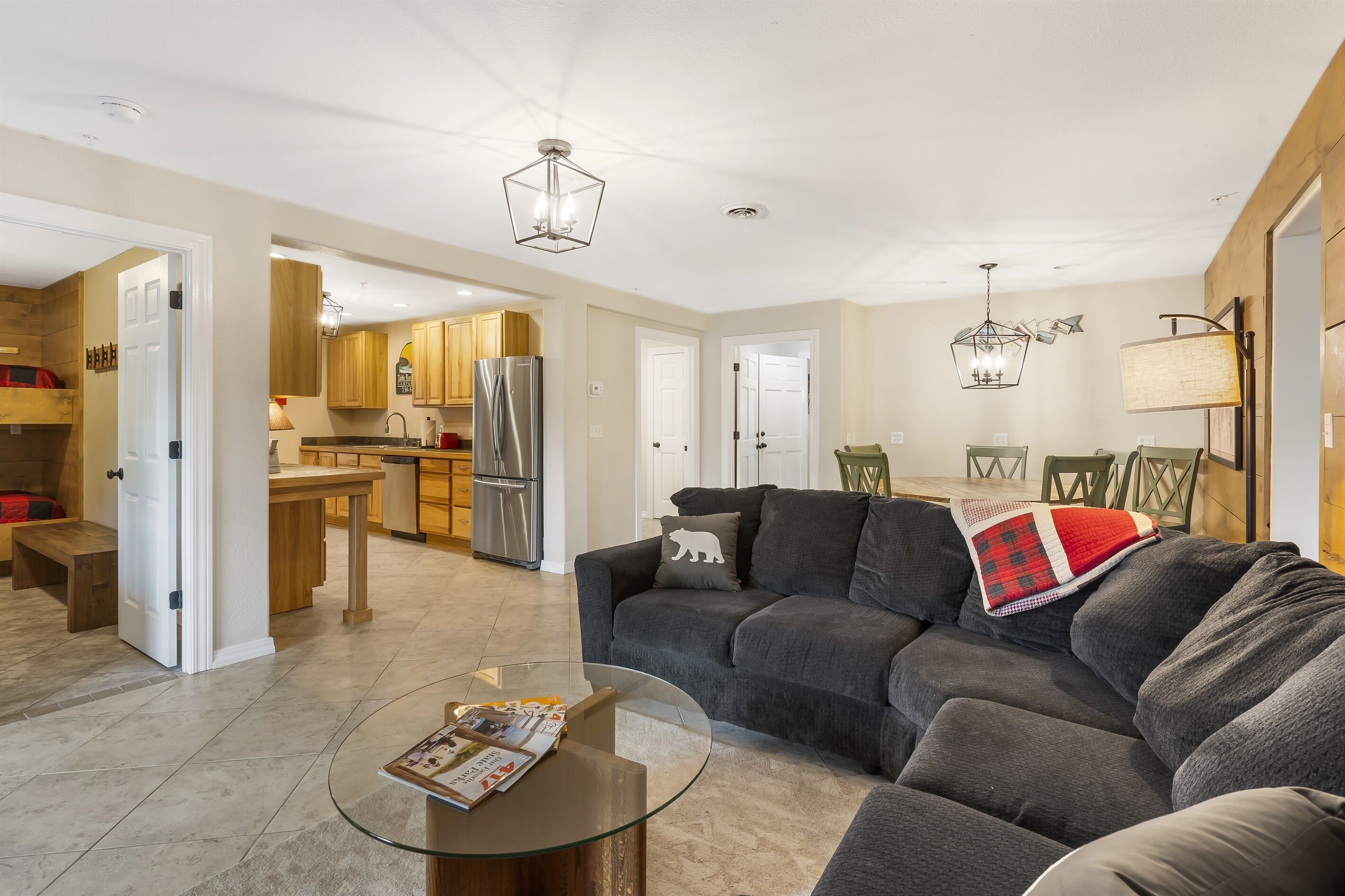 A modern living room with a gray sectional sofa, a glass coffee table, and a kitchen in the background.