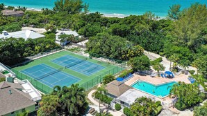 A tennis court surrounded by lush greenery and a pool area with lounge chairs.