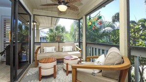 A covered outdoor seating area with a sofa, chairs, and a table, overlooking a lush garden.