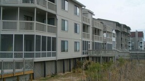 Un edificio residencial de varios pisos con balcones, ventanas amplias y una zona de terraza de madera.