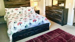 Une chambre à coucher avec un lit, une commode, une table de chevet, une lampe et une porte.