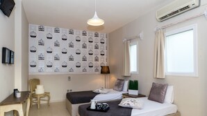 A hotel room with two beds, a desk, a chair, a wall with a bird pattern, a window with curtains, and an air conditioning unit. - Boutique studio for 2pers. (109) (Malia)