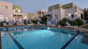 A swimming pool with tiled flooring, surrounded by lounge chairs and umbrellas, and adjacent to a building with multiple balconies and windows. - Boutique studio for 2pers. (109) (Malia)